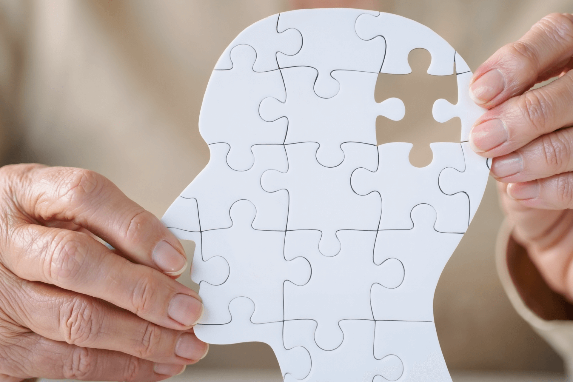 El Parkinson: una enfermedad que nos invita al trabajo en equipo 1 Manos de adulto mayor sosteniendo una figura de cabeza humana en forma de rompecabezas incompleto, simbolizando deterioro cognitivo y enfermedades neurológicas.