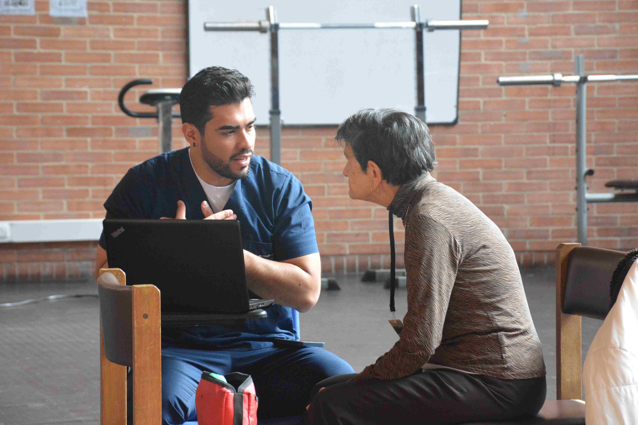 Estudiante de salud conversando con paciente adulta mayor durante consulta de rehabilitación, ECR